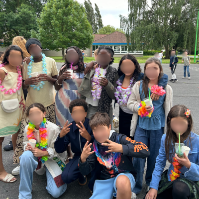 Un groupe d'élèves de CM2 portant des colliers de fleurs colorés posent ensemble de manière festive dans la cour de l'école lors de leur bal de fin d'année.