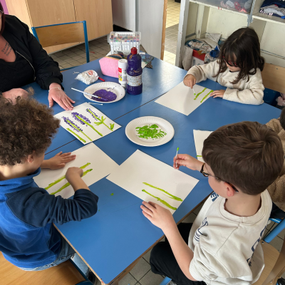 Trois enfants du centre de loisirs peignent des fleurs de printemps en utilisant des cotons-tiges lors d'un atelier créatif autour d'une table bleue