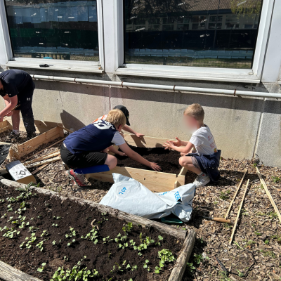 Deux garçons du centre de loisirs remplissent de terreau un carré potager en bois avec leurs mains lors d'un projet de jardinage en extérieur.