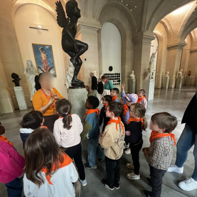 Un groupe d'enfants du centre de loisirs portant des foulards orange écoute attentivement une guide devant une statue en bronze au Palais des Beaux-Arts de Lille.